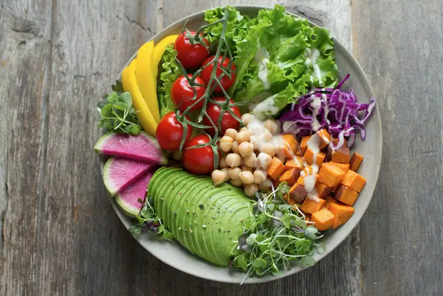 A colourful grain bowl with roast vegetables, avocado and herbs
