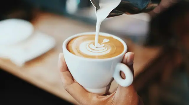 Steamed milk being poured into a latte, forming a rosetta